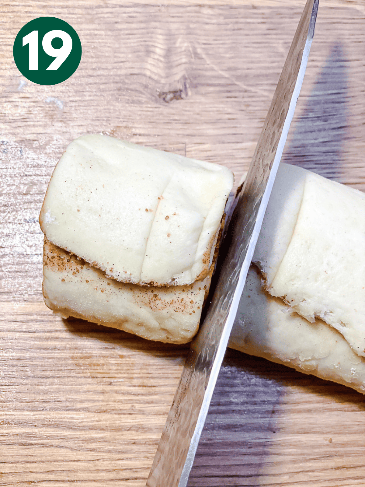 close up on a knife slicing a cinnamon roll from a log of dough.