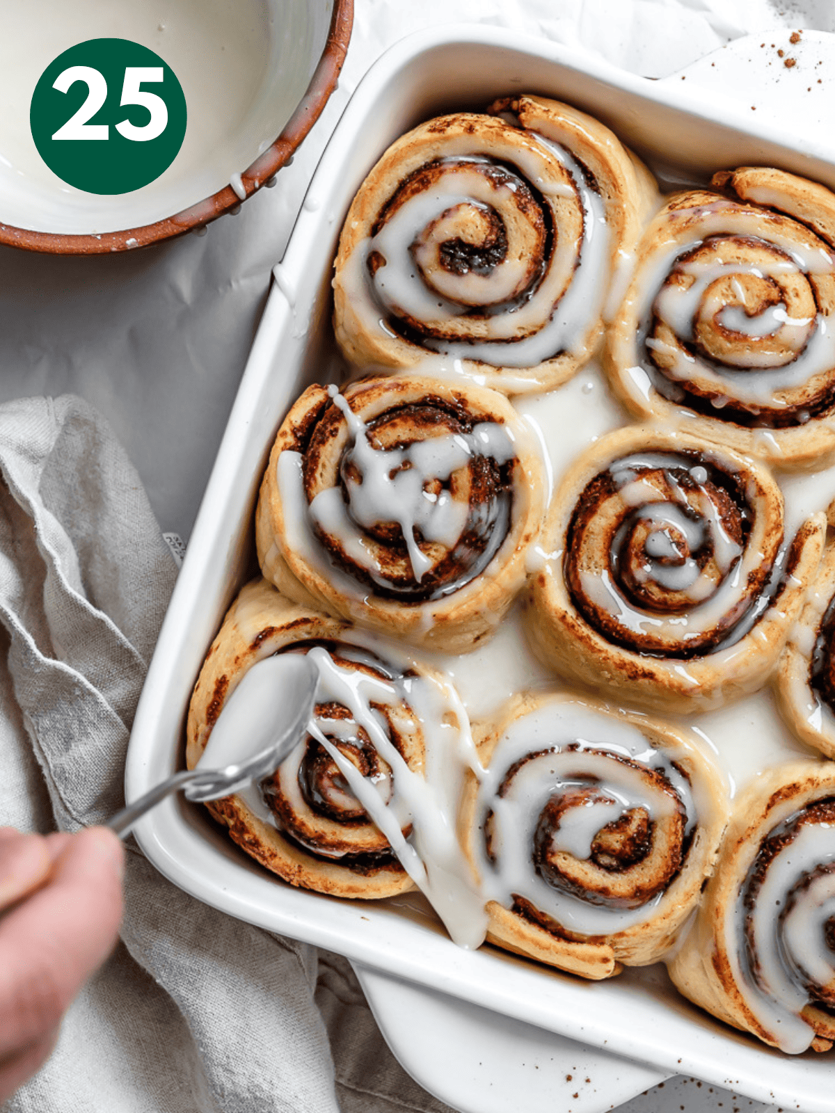 drizzling vanilla icing over vegan cinnamon rolls.