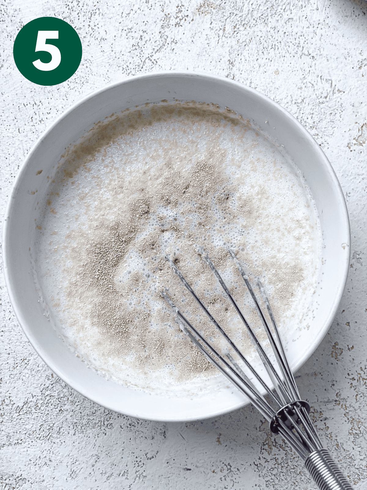 whisking yeast into vegan buttermilk in a white bowl.