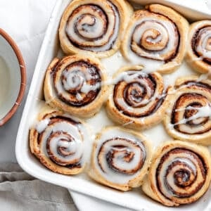 vegan cinnamon rolls in a white baking pan with vanilla icing on top.