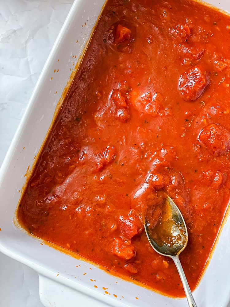 marinara sauce spread on the bottom of a baking dish.