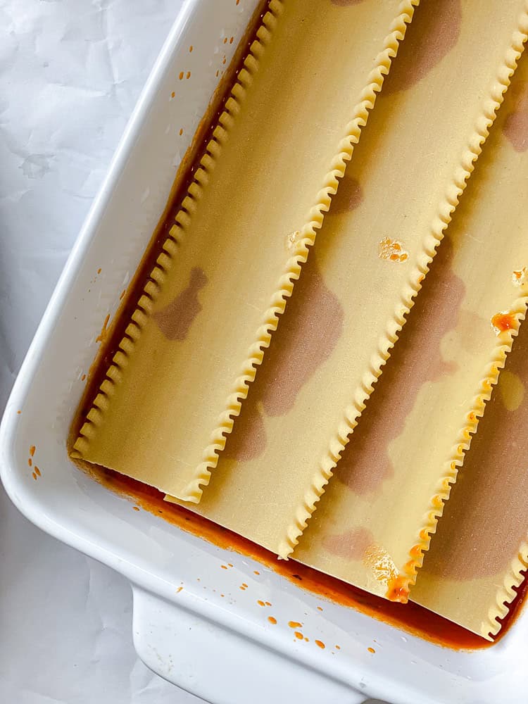 lasagna noodles layered over marinara sauce in a baking dish.