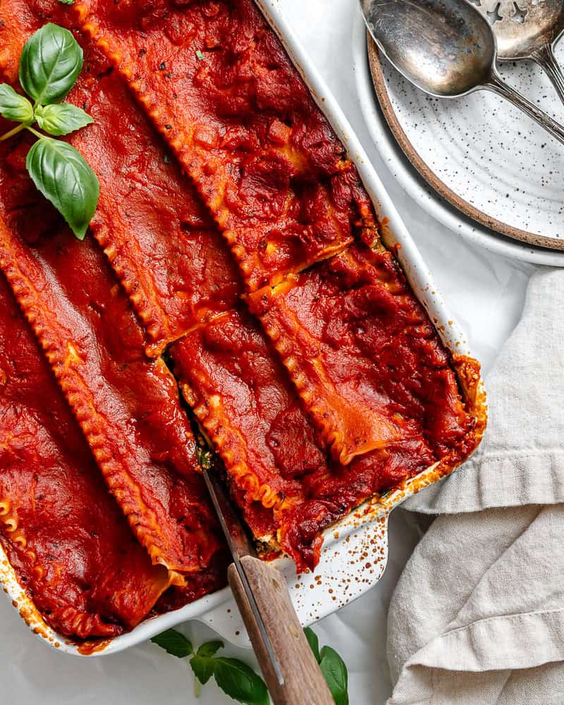 cutting a slice of vegan lasagna in a baking dish.