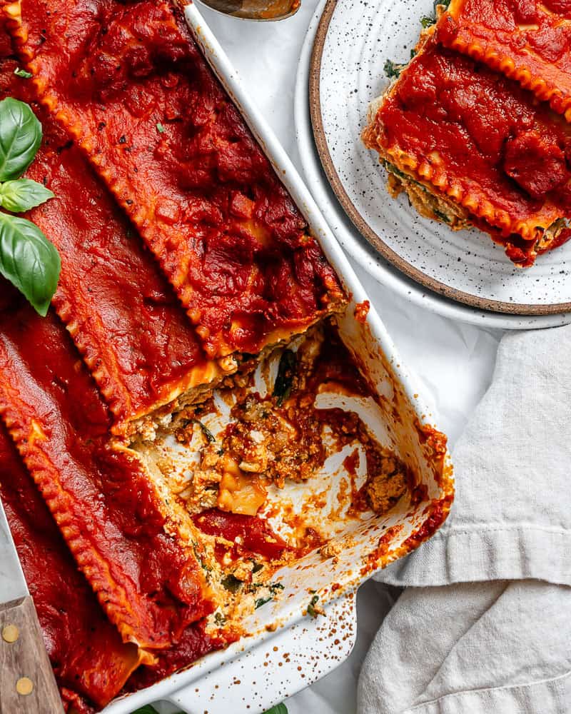 vegan lasagna in a white baking dish with a slice on a separate plate