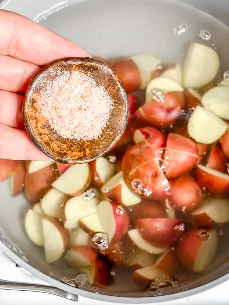 pouring salt into a pot with water and chopped red baby potatoes.