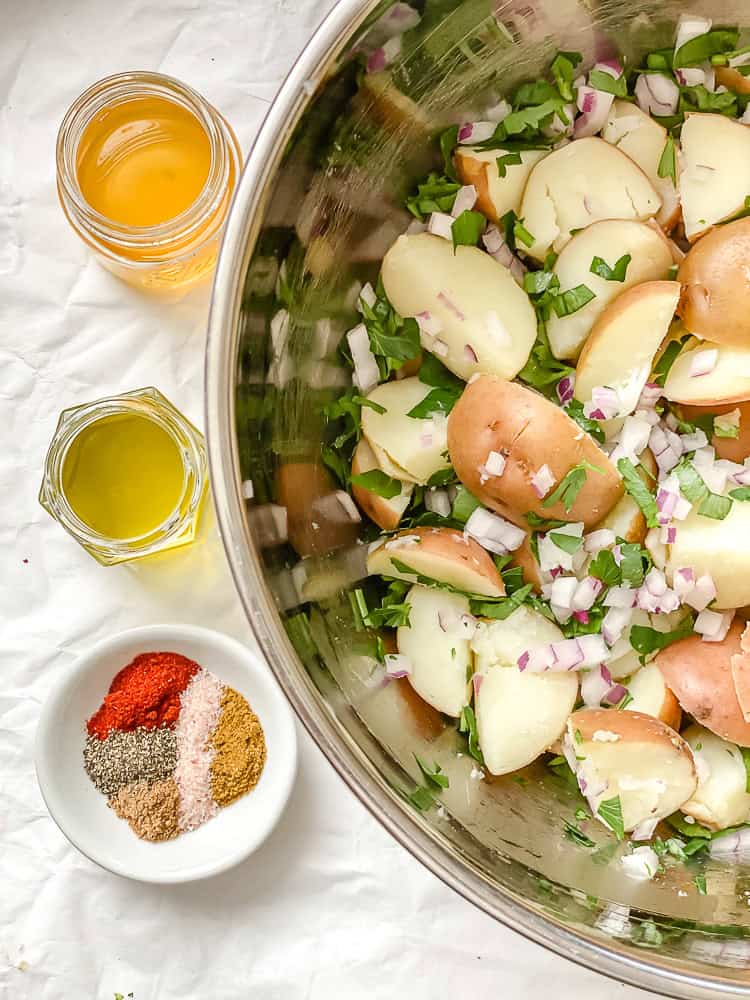 spices, oil, and vinegar in jars next to a bowl of French potato salad.