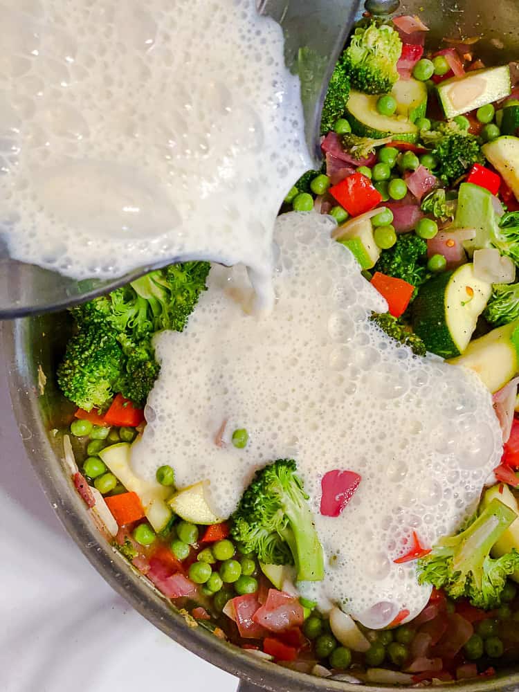 pouring cream sauce into a pot with vegetables.