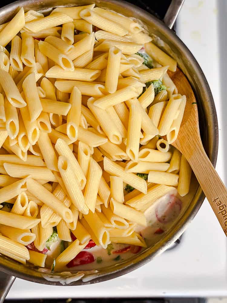 using a wooden spoon to toss cooked veggies in a pot with a cream sauce and vegetables.